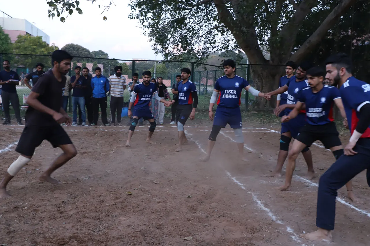 Kabaddi players lunge to tackle a raider on the mud court