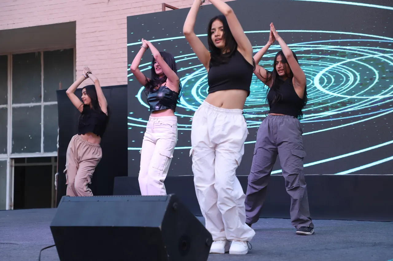 Four dancers perform in sync on stage in front of an LED screen