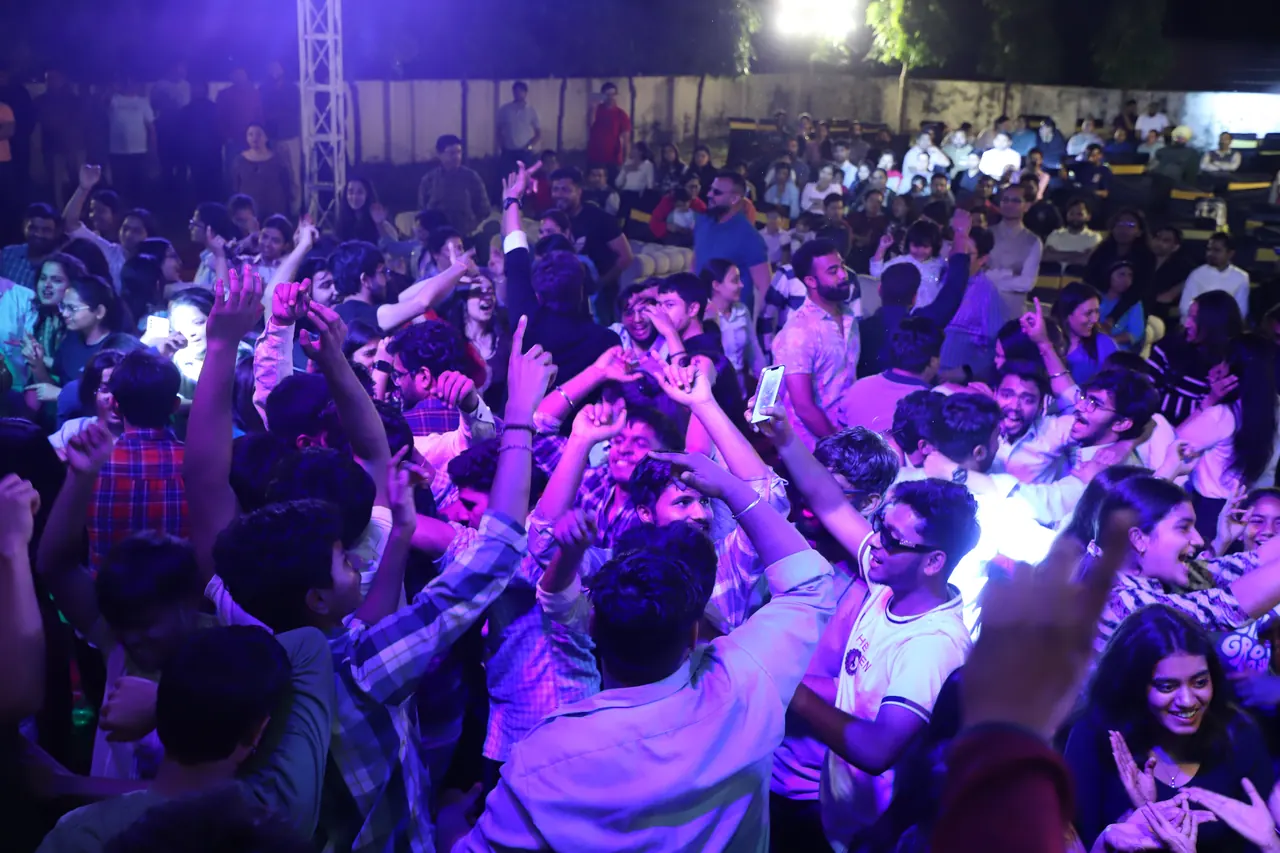 A dense crowd dances under purple and blue lights during an evening programme